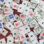 Close-up of scattered Deco mahjong tiles showing pink characters, blue dots, green bamboo, and floral tile backs.