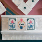 Close-up of two pink floral Deco mahjong tiles flanking a joker in a pearlescent white rack.