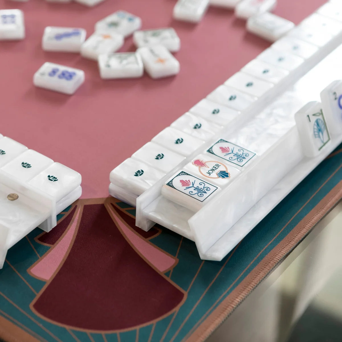 Mother-of-pearl-patterned Deco tiles and white racks on a pink mahjong mat, with flower and joker tiles in front.