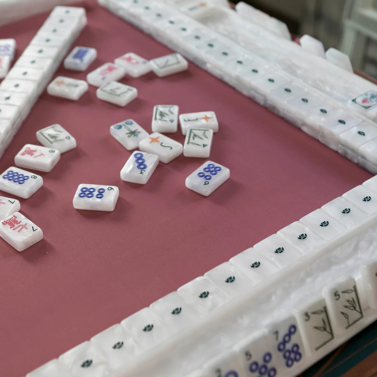 Deco mahjong game on a pink mat with scattered tiles, stacked walls, and pearlescent white racks.