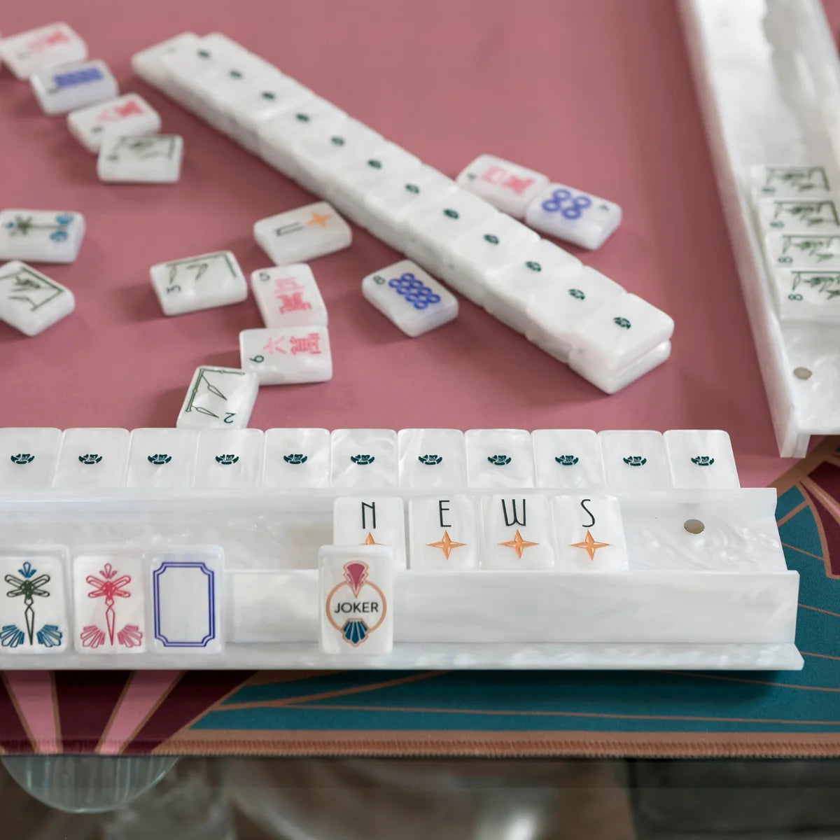 Deco wind, dragon, and joker tiles displayed in a pearlescent white rack on a pink mahjong mat.